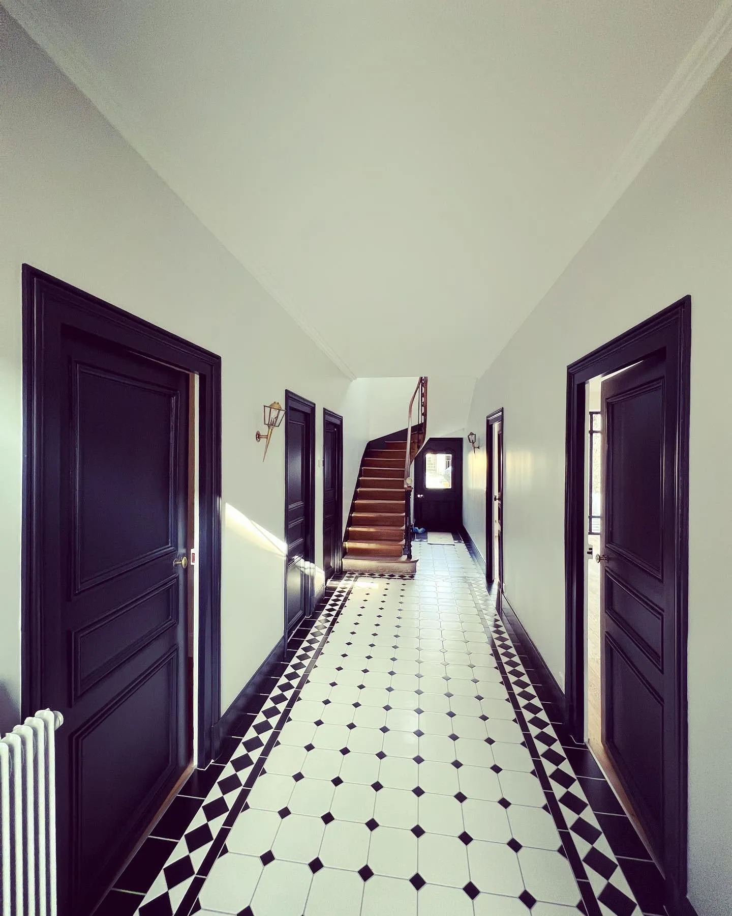 Couloir avec portes noires et escalier en bois, après rénovation
