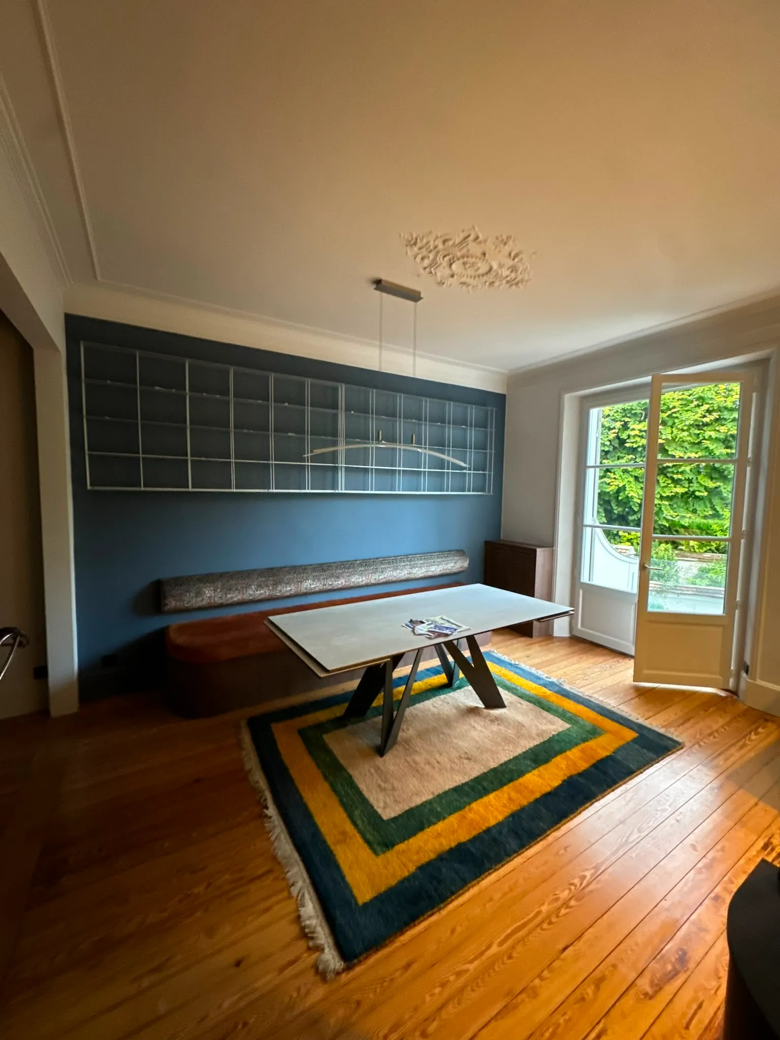 Salle à manger rénovée avec mur bleu, banquette et tapis coloré